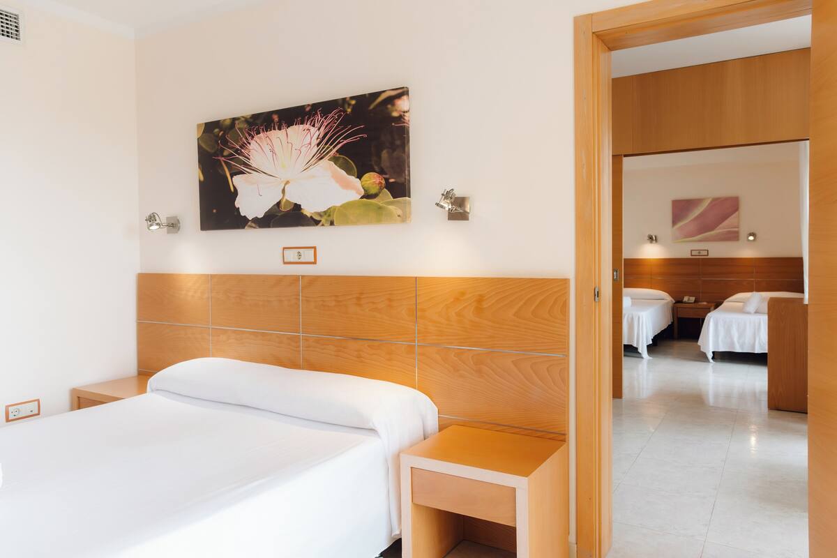 A hotel room with a large bed, a bedside table, a nightstand, a wall-mounted lamp, and a painting of a flower.
