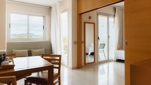 A modern hotel room with a dining area, a large window with a view, and a sliding door leading to a balcony. - Bluesea Salina (Santa Eulalia del Rio)