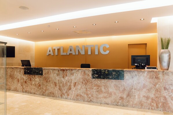 A reception desk with the word "ATLANTIC" prominently displayed, a flat-screen TV, and a potted plant. - Bluesea Salina (Santa Eulalia del Rio)