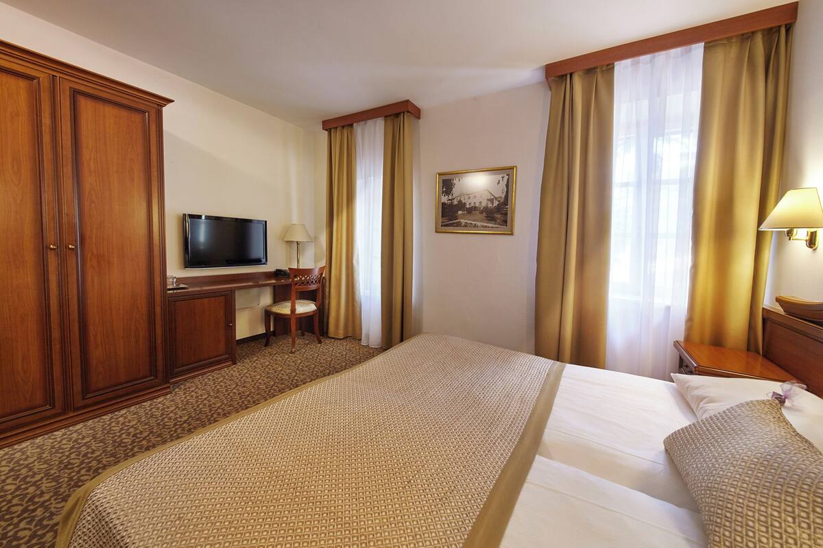 A hotel room with a large bed, a desk with a flat-screen TV, a chair, and a picture on the wall.