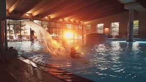 Una piscina interior con cascada, rodeada de sillones de descanso y amplias ventanas.