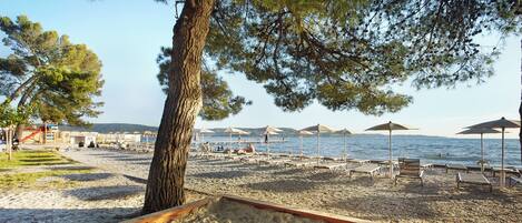 A beach with sun loungers and umbrellas, a playground, and a view of the water.