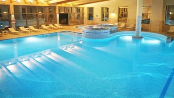 Une grande piscine intérieure dotée de chaises longues et d’un espace avec un bain à remous.