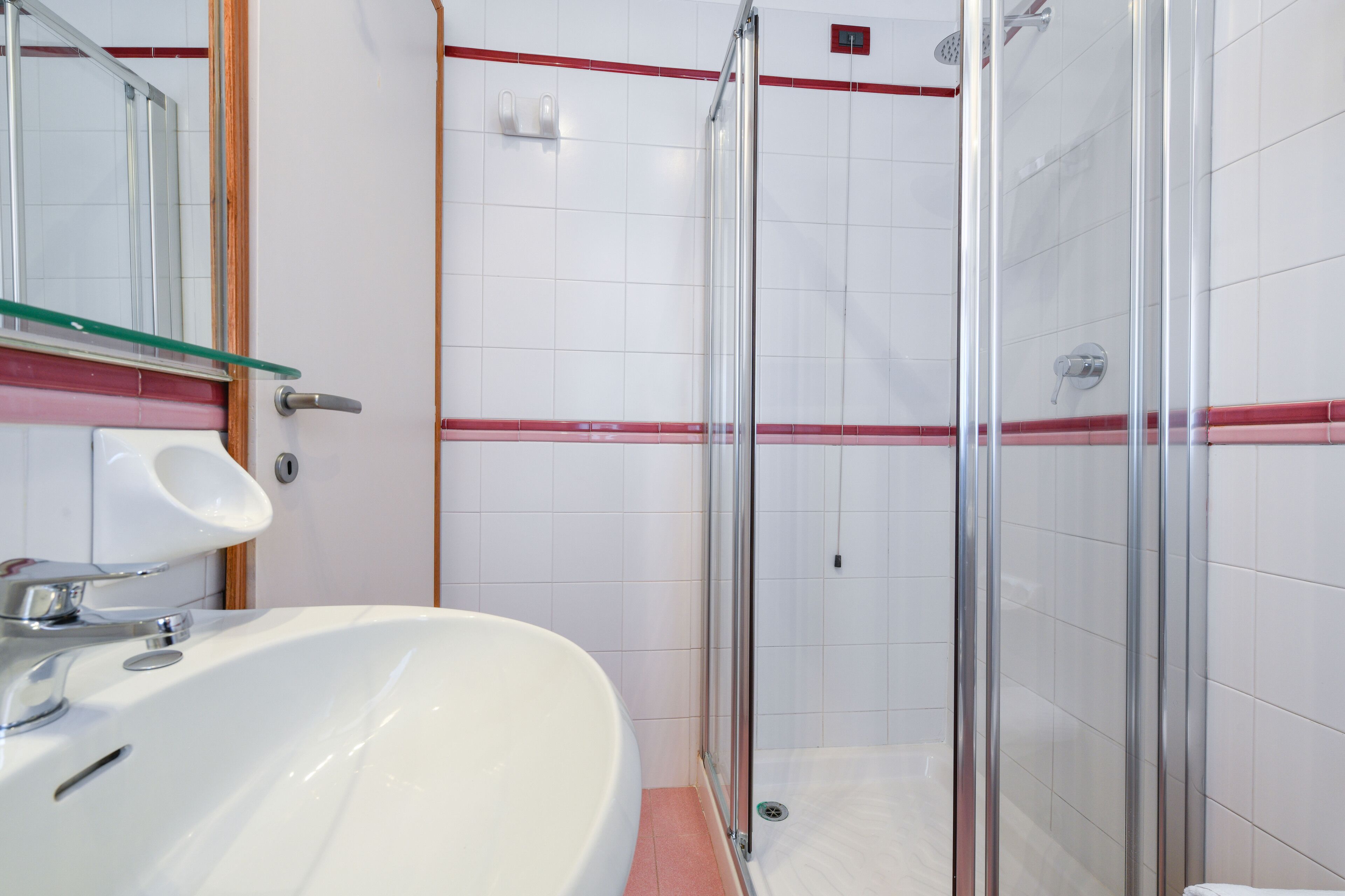 A bathroom with a white sink, glass shower enclosure, and a red stripe on the wall.