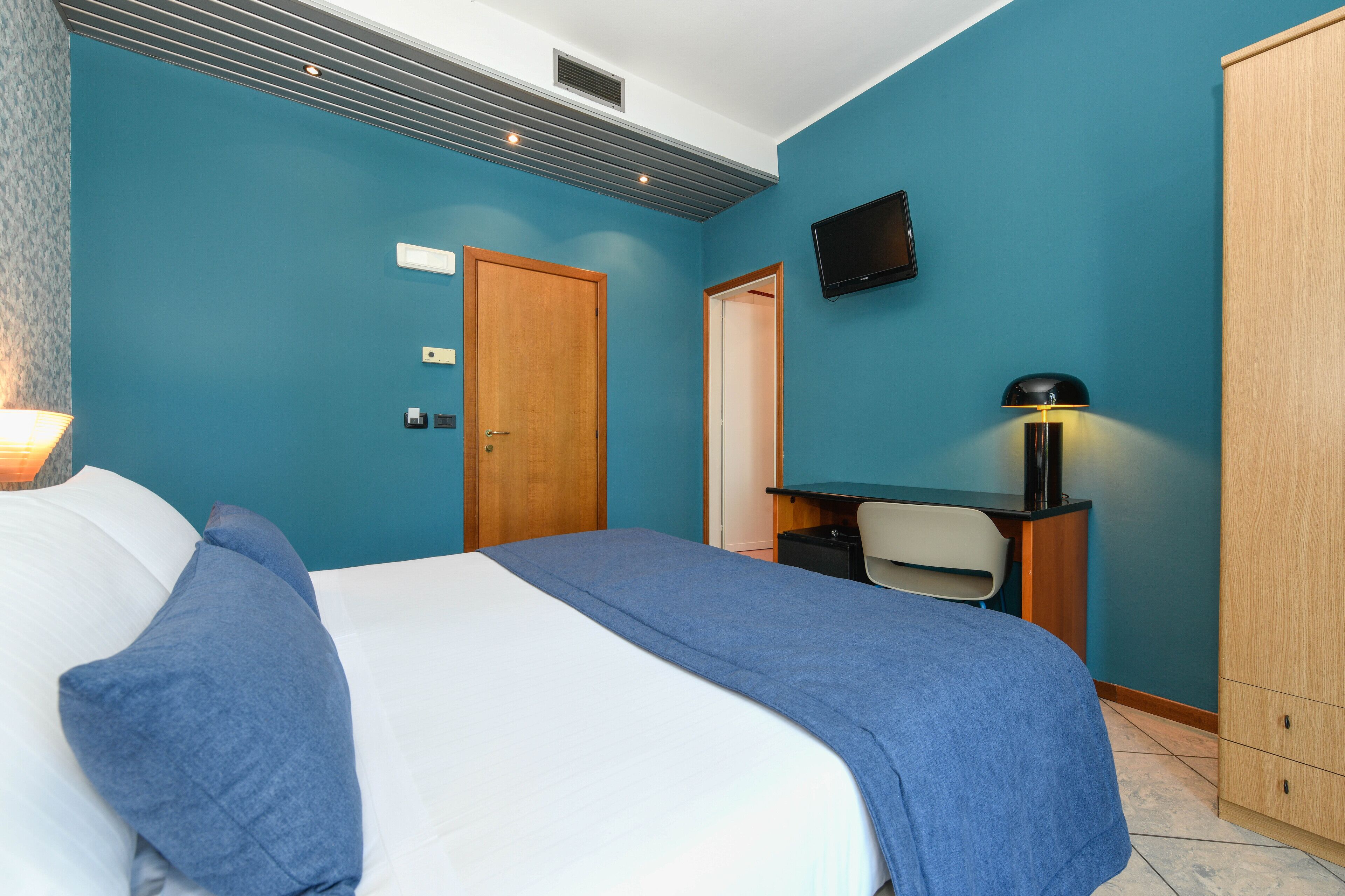 Une chambre à coucher comprenant un lit, un bureau, une chaise, un téléviseur et une armoire.