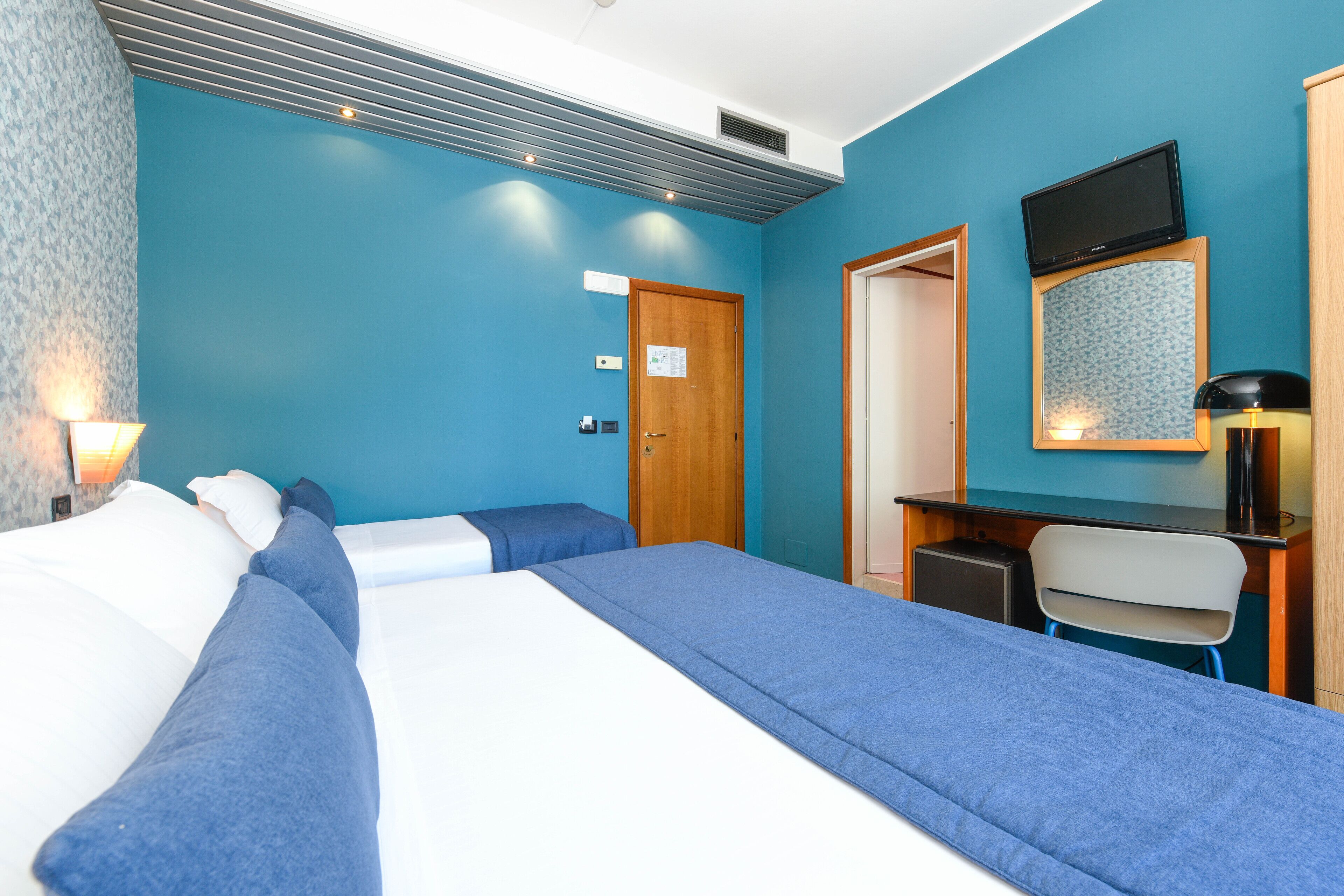 Habitación de hotel con dos camas, un escritorio, una silla, un televisor y una puerta.
