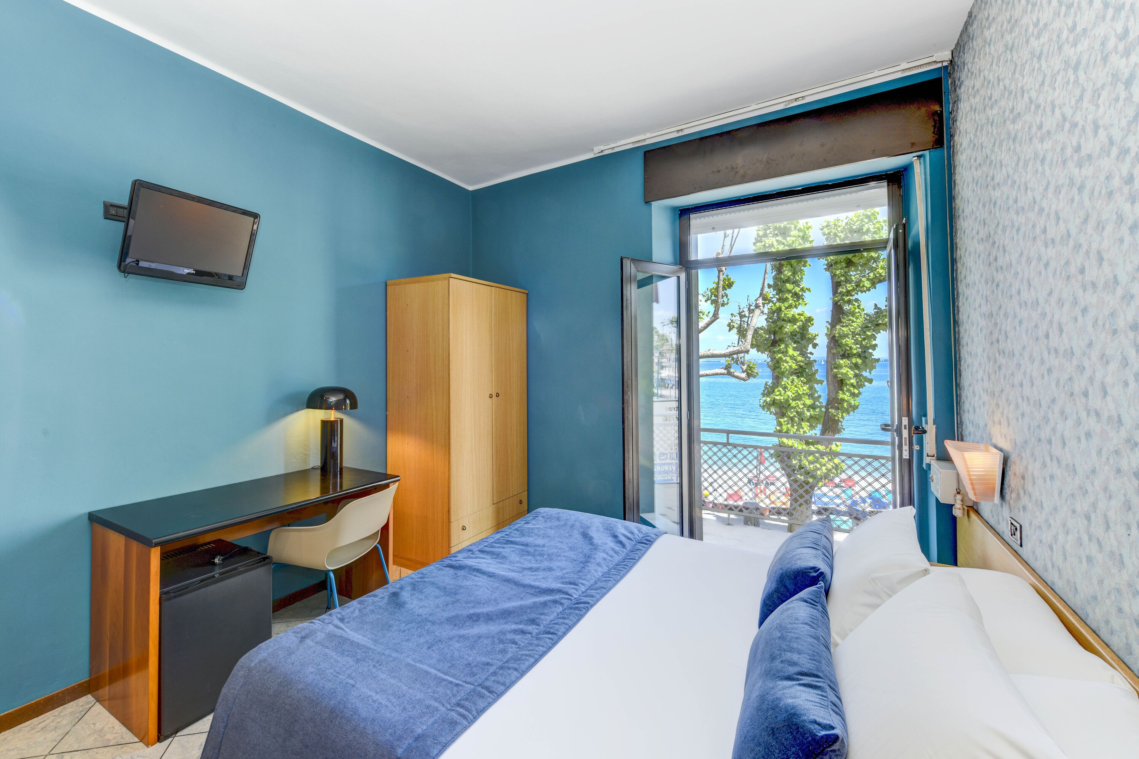 A hotel room with a bed, a desk, a chair, a wardrobe, and a TV.