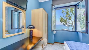 Una stanza con una scrivania in legno, una sedia, un letto, un armadio, una TV montata a parete e una finestra vista mare.