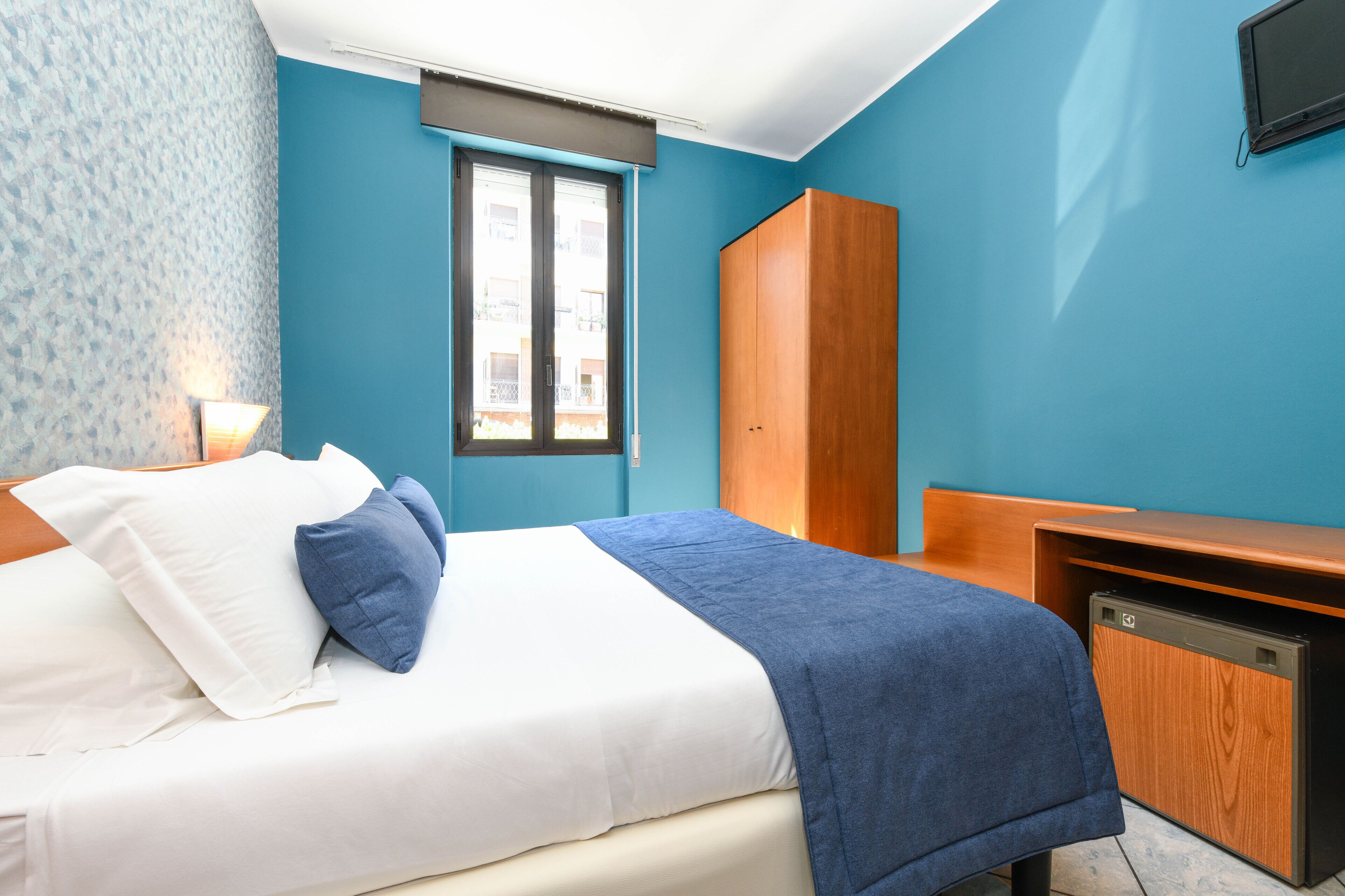 A bedroom with a bed, a wardrobe, a desk, and a window.
