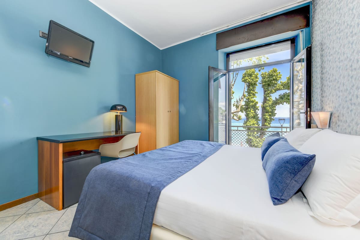 A bedroom with a bed, a desk, a chair, a wardrobe, and a TV on the wall.