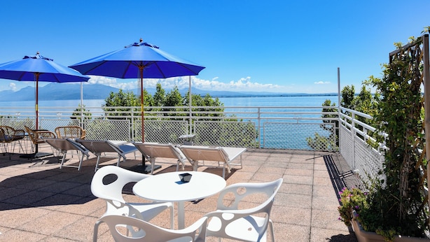 Una terrazza con sedie e tavoli bianchi, ombrelloni blu e vista sul mare.
