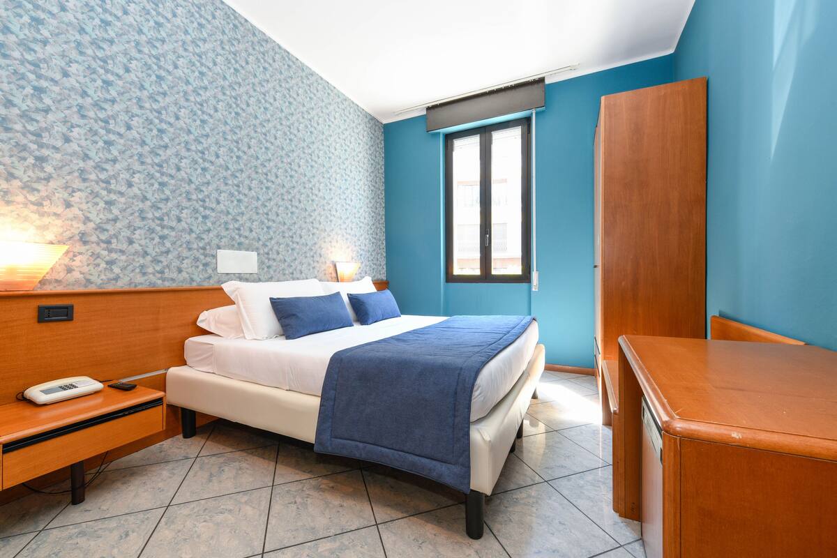 A bedroom with a bed, bedside table, lamp, and wardrobe.