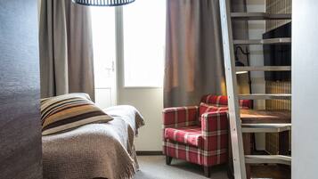 Une chambre à coucher avec un lit, un fauteuil à motifs écossais, une étagère en bois et une fenêtre avec des rideaux.