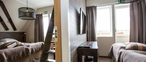 Habitación de hotel con dos camas, un escritorio, una silla, una lámpara colgante y una ventana con cortinas.