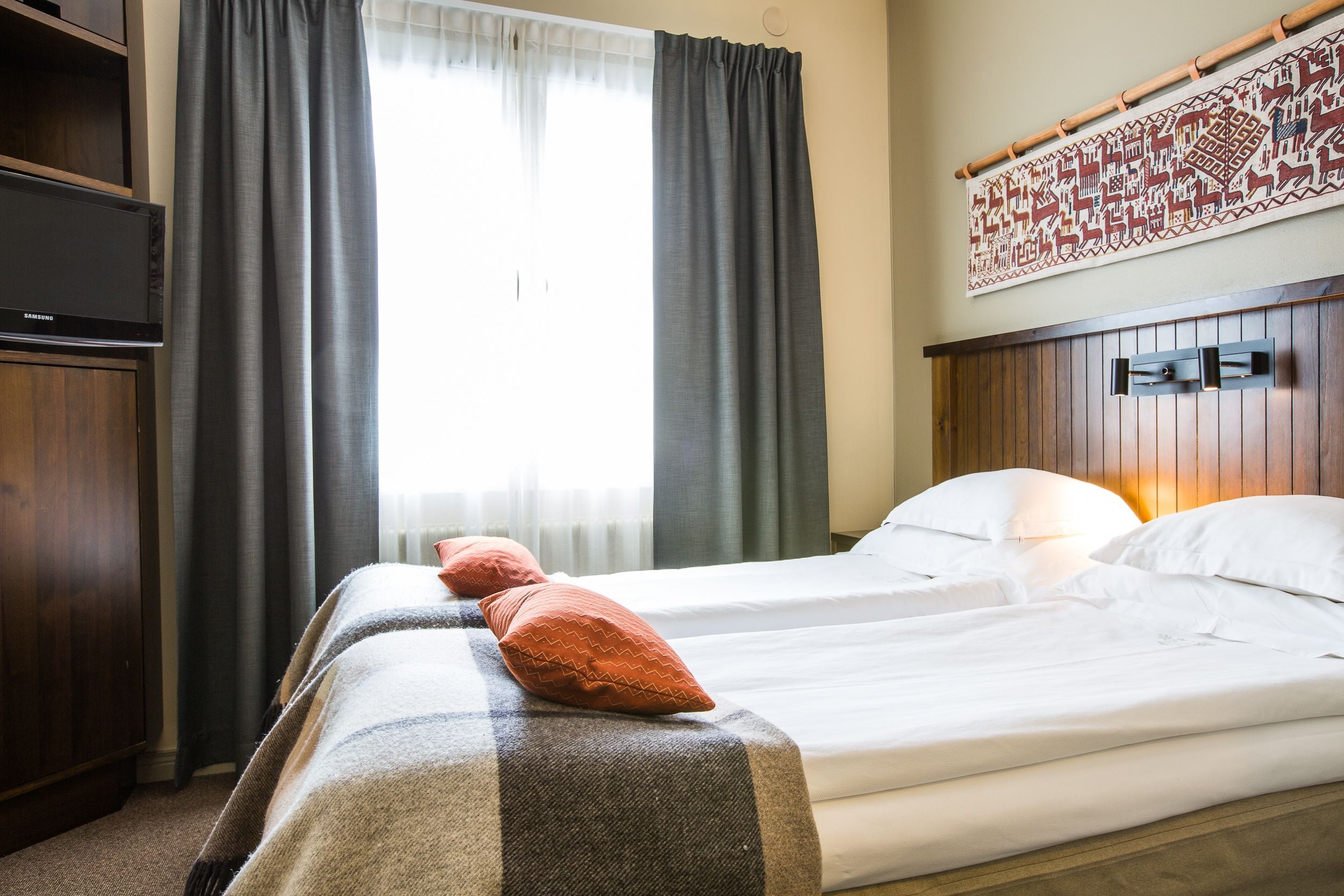 Et hotelværelse med seng, fjernsyn og et vindue med gardiner.