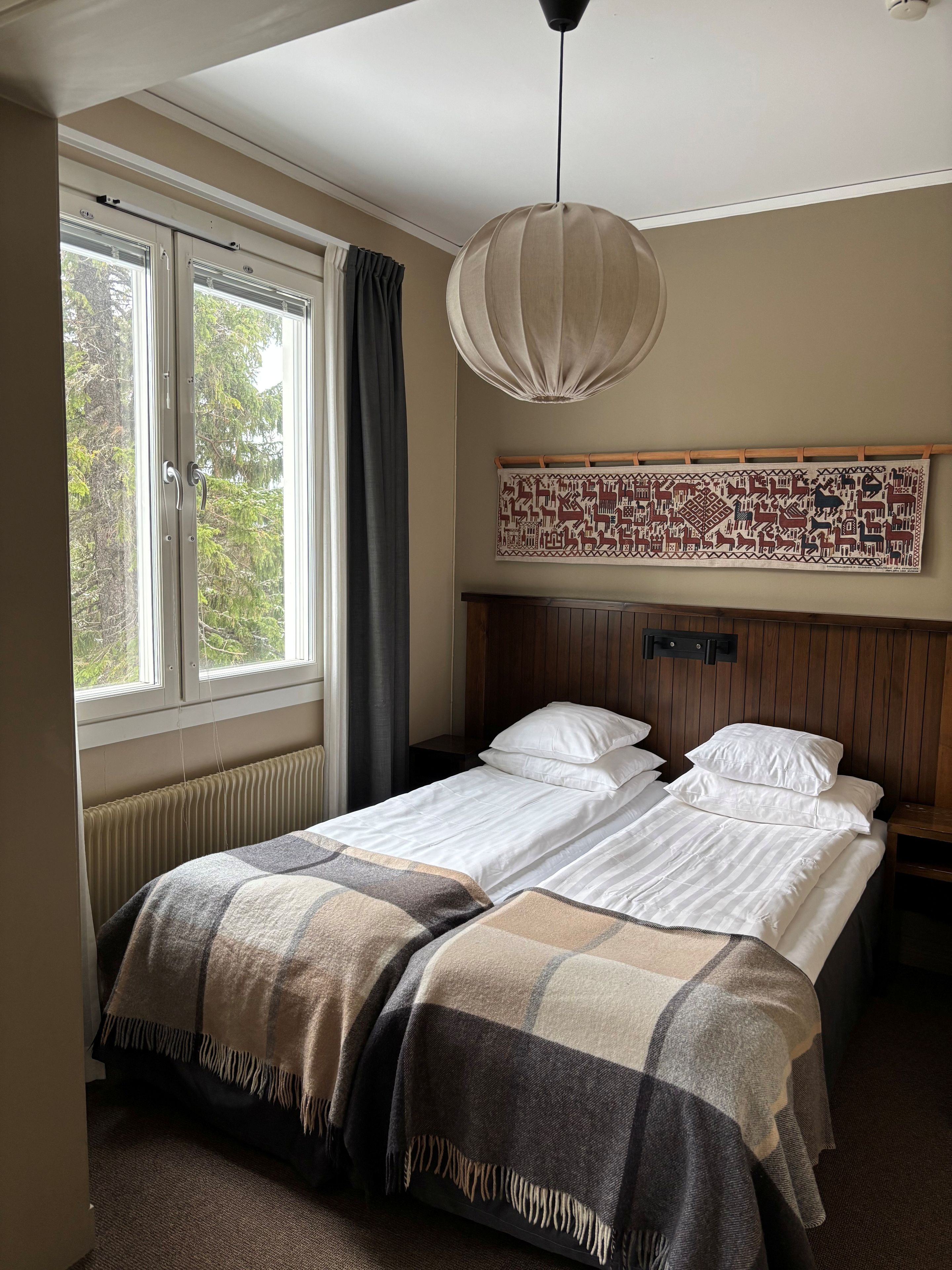 A room with a bed, a window with curtains, a hanging light fixture, and a wall-mounted tapestry.