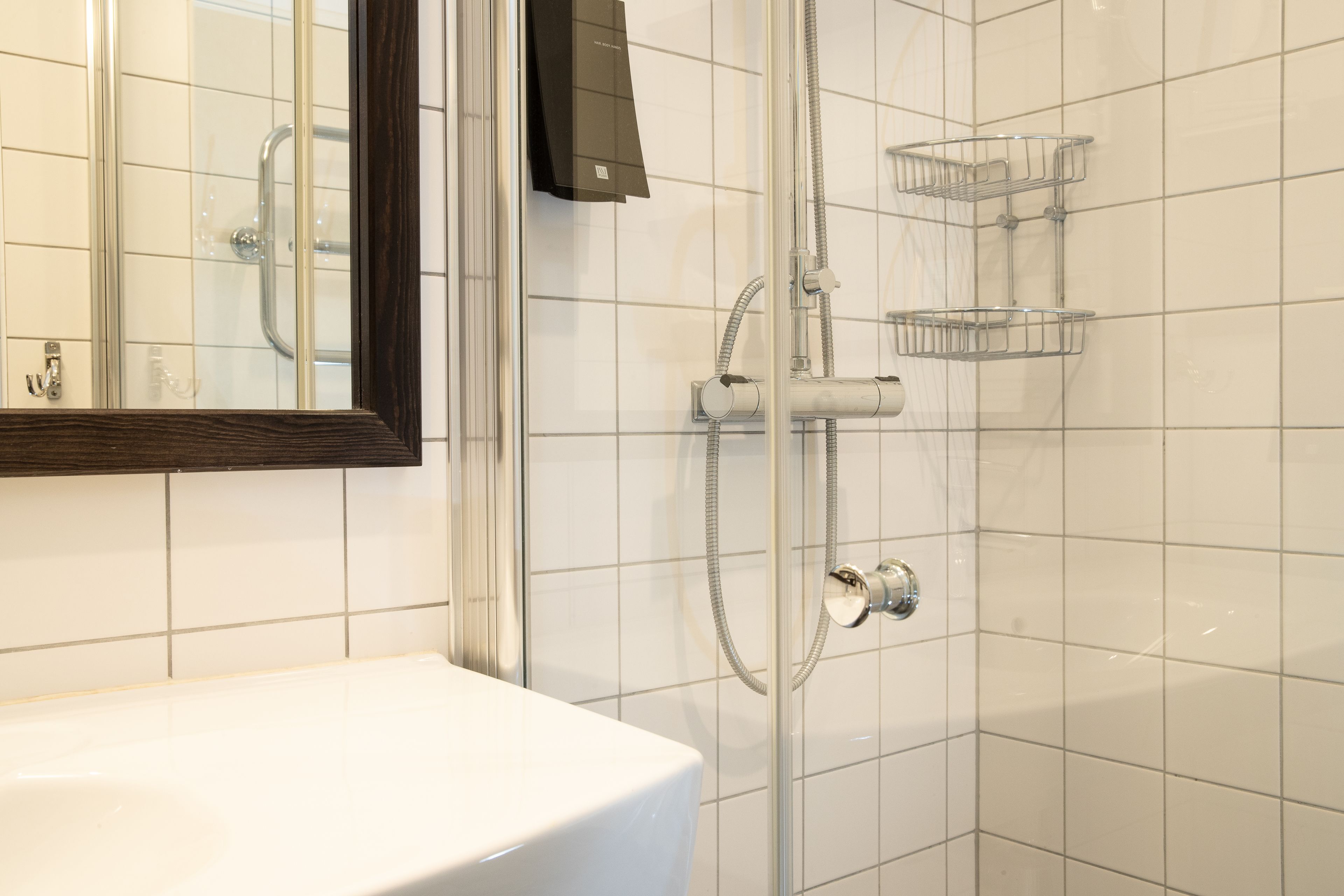 Une salle de bain avec un lavabo blanc, une douche en verre et un miroir.