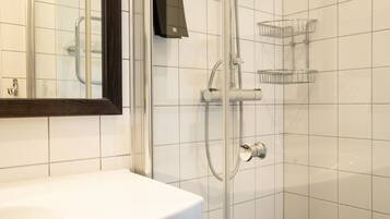 Une salle de bain avec un lavabo blanc, une douche en verre et un miroir.