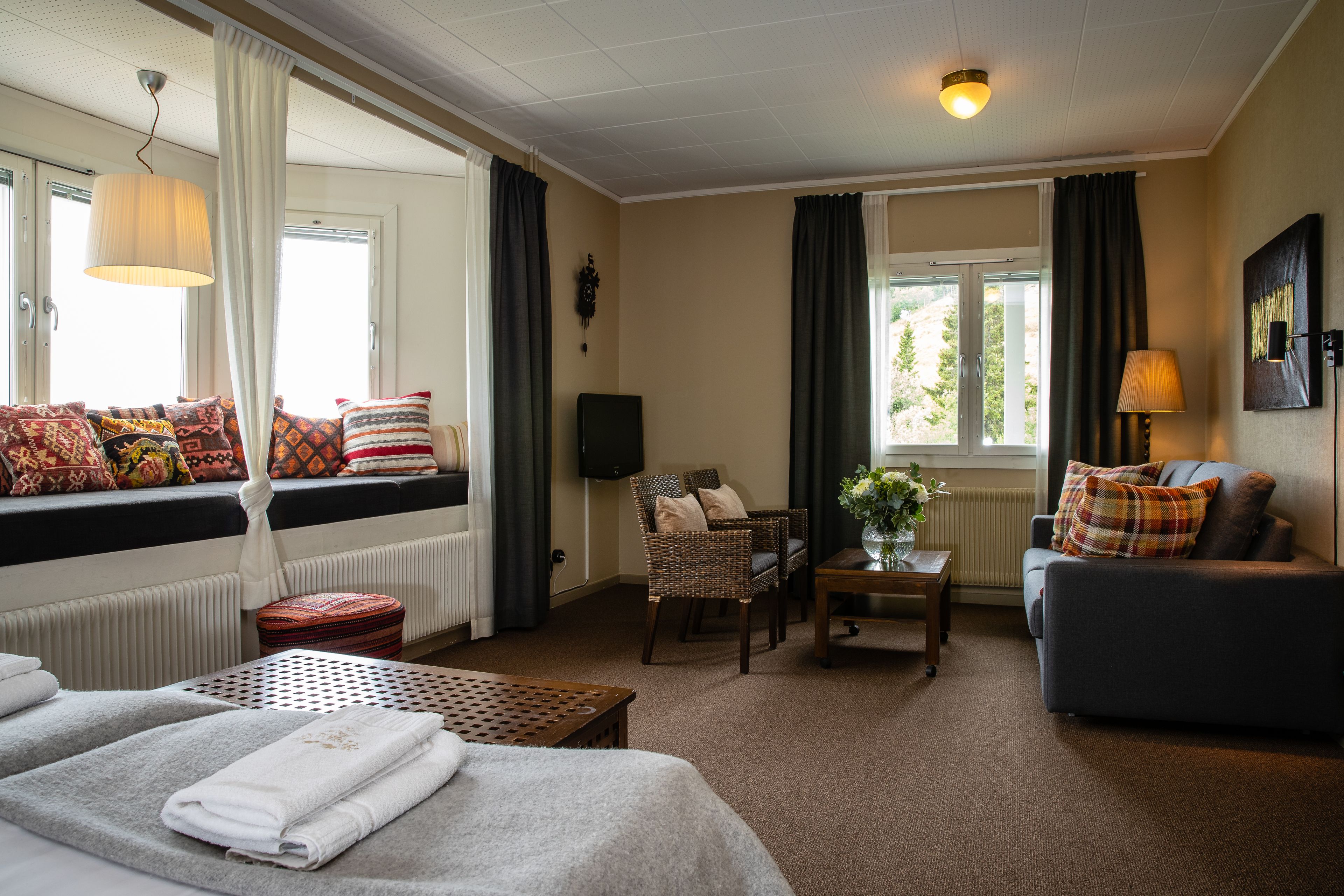 A hotel room with a bed, a sofa, a chair, a small table with a vase, and a window with curtains.