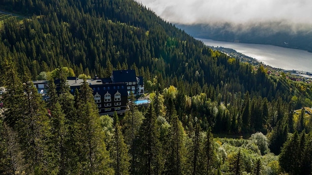 A large building surrounded by dense forest, overlooking a lake.