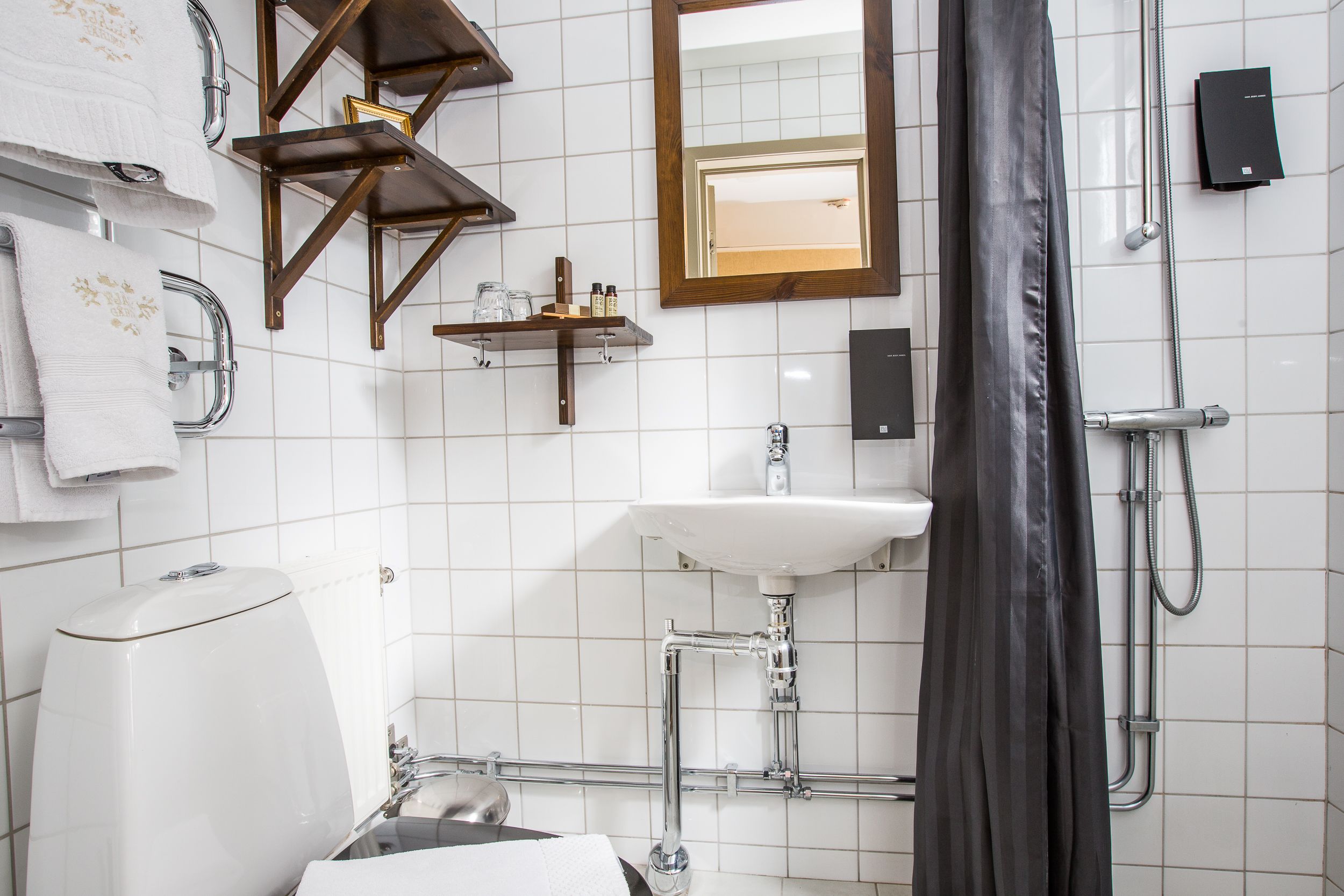 A modern bathroom with a white sink, chrome fixtures, a shower with a black curtain, and a mirror with a wooden frame.