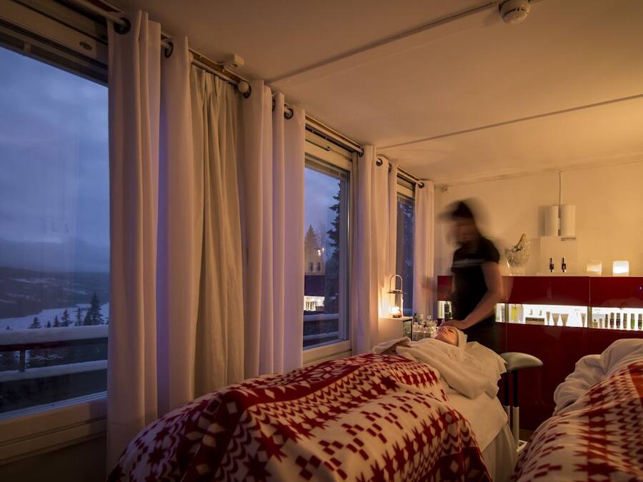 Een hotelkamer met twee bedden, een groot raam met gordijnen, een nachtkastje met lamp en uitzicht op een besneeerd landschap.