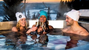 Three people in a hot tub with a scenic view of trees and a sunset in the background.