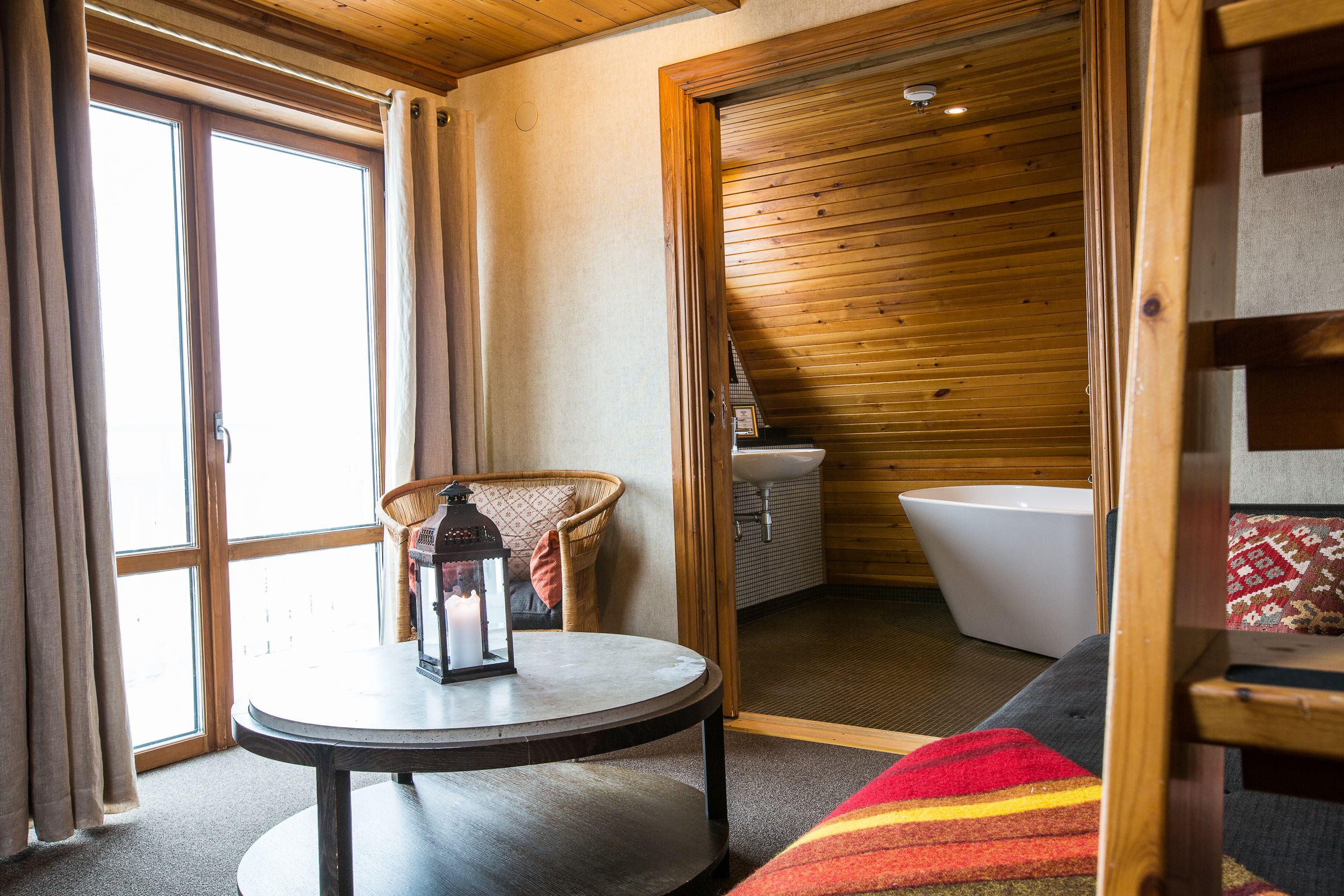 Una habitación acogedora con una mesa redonda, una silla de mimbre, una bañera y una ventana con cortinas.