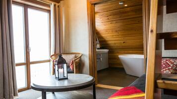A cozy room with a round table, a wicker chair, a bathtub, and a window with curtains.