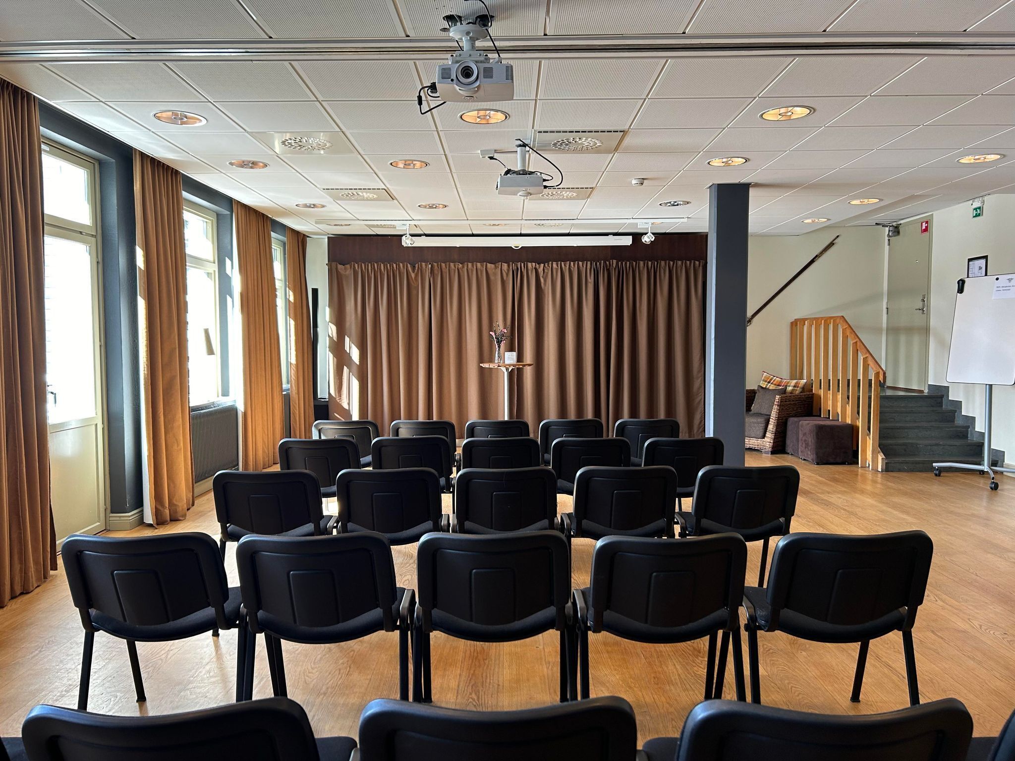 Un salón de conferencias con filas de sillas, un proyector y una pizarra.