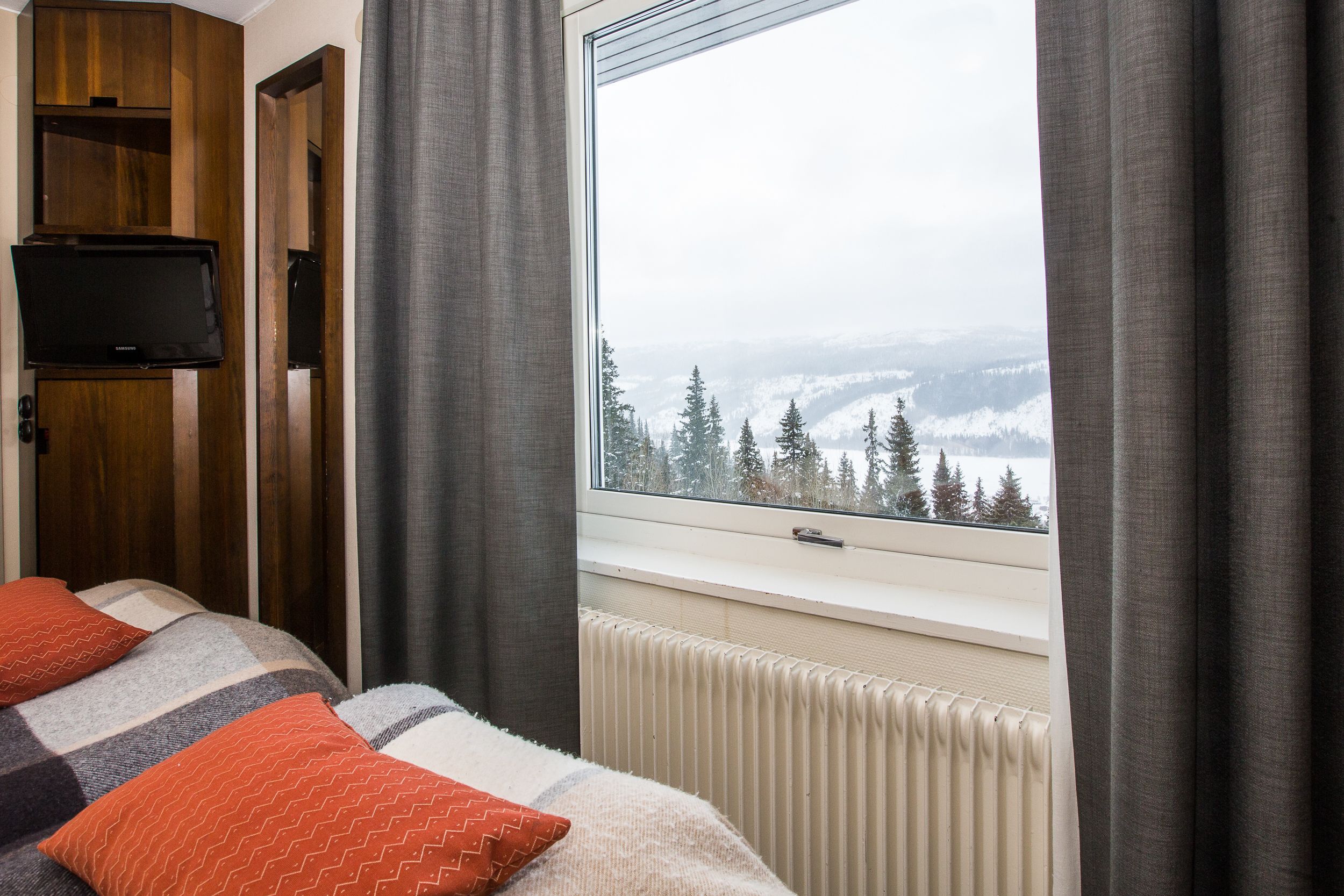 Une chambre à coucher avec un lit, un téléviseur fixé au mur et une fenêtre donnant sur un paysage enneigé.