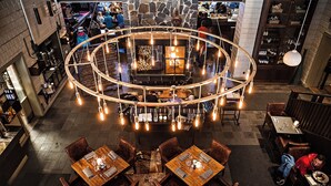 A circular bar area with hanging lights and a central fireplace, surrounded by wooden tables and chairs.