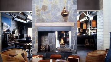 A cozy lounge area with a stone fireplace, wicker furniture, and a bar in the background.
