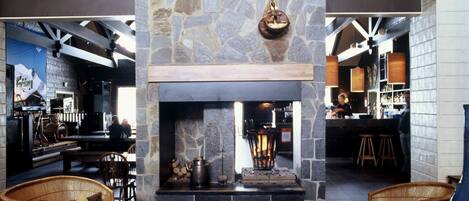 A cozy lounge area with a stone fireplace, wicker furniture, and a bar in the background.
