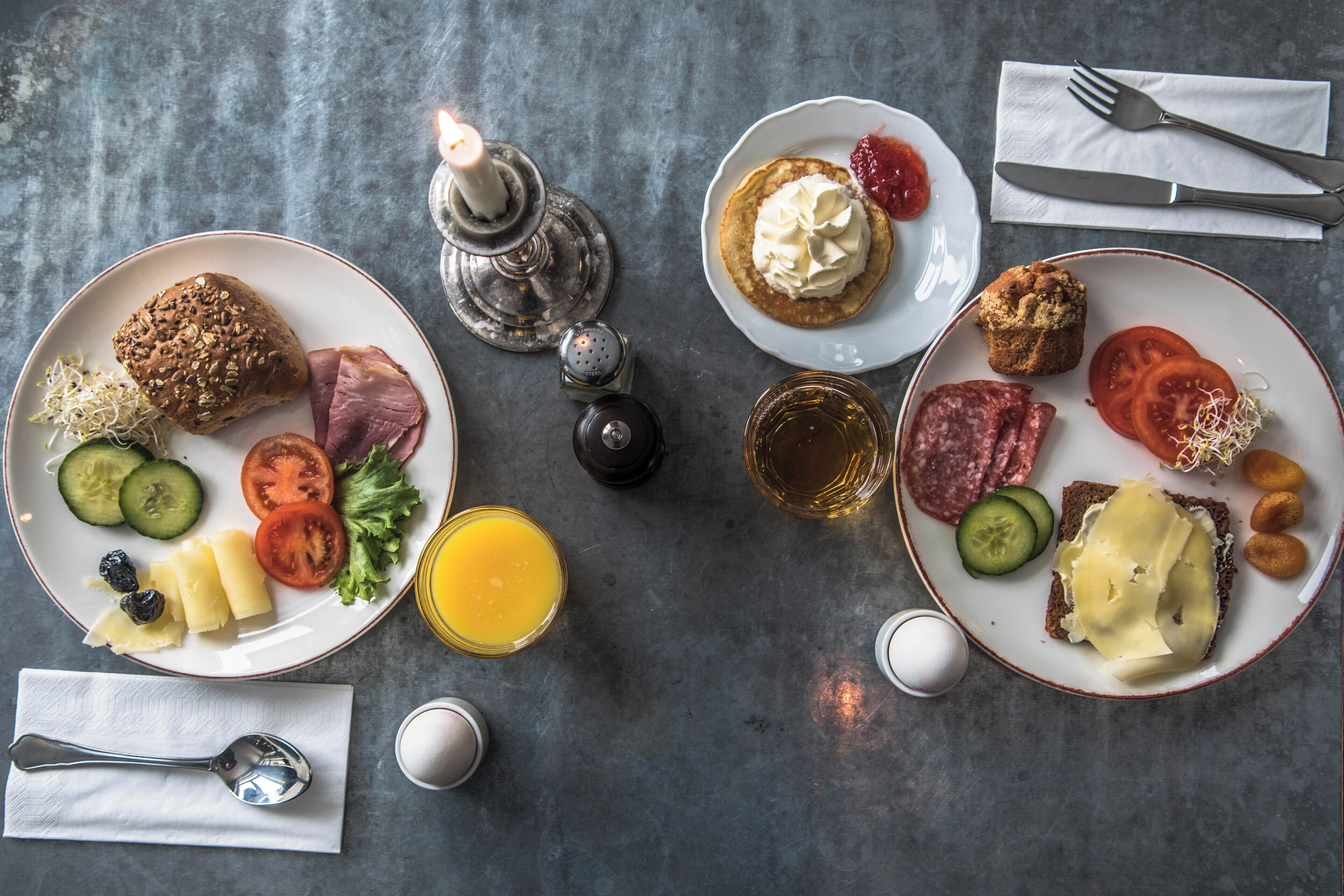 Two plates with various breakfast items, a candle, salt and pepper shakers, a fork and knife set, and a glass of orange juice on a table.