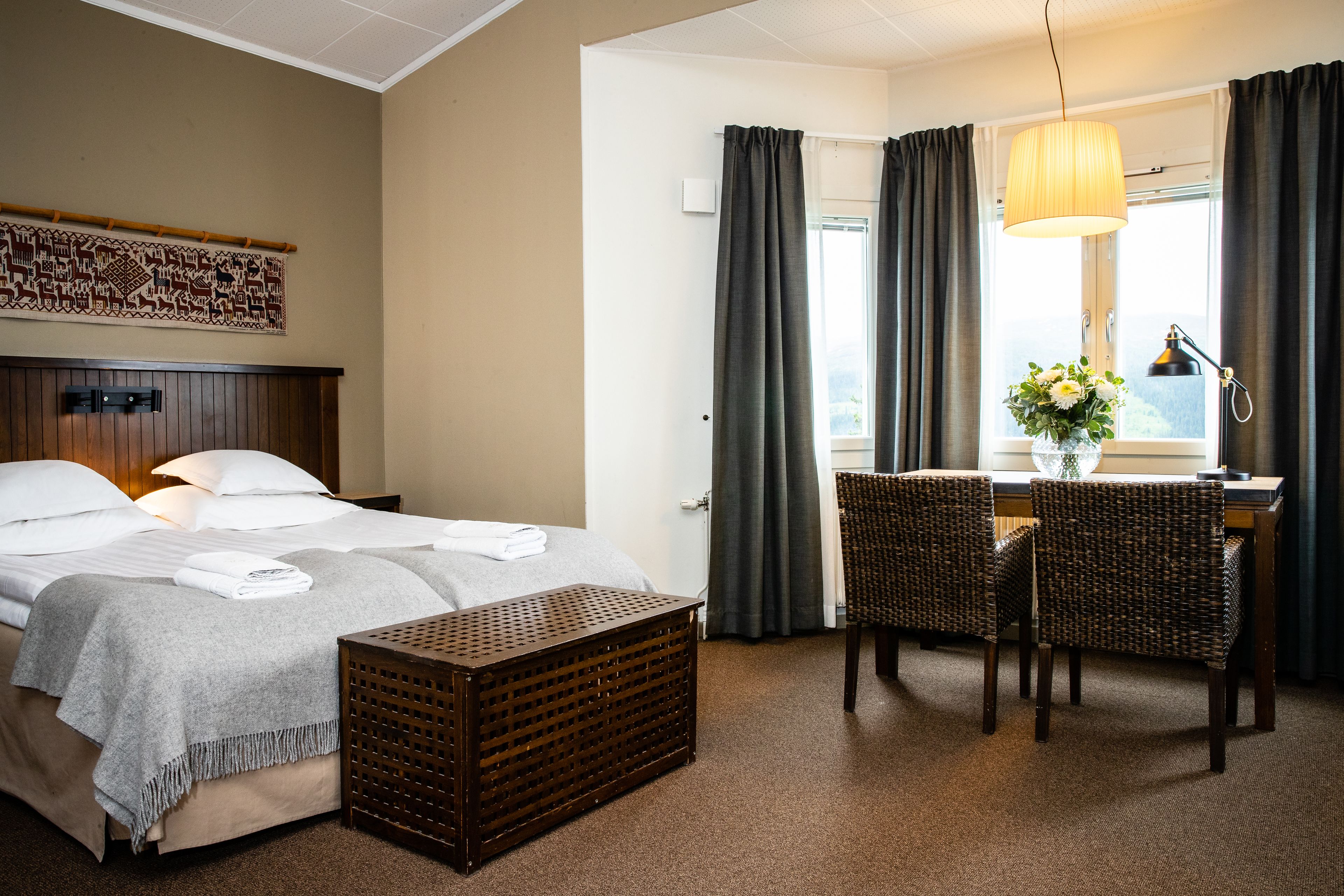 A hotel room with a bed, a desk with a chair, a lamp, and a window with curtains.