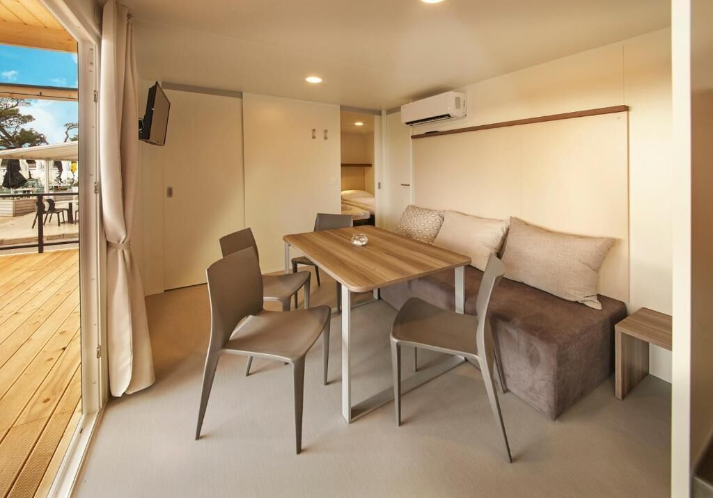 Une pièce de taille modeste, avec une table et des chaises en bois, un canapé avec des coussins, une petite table de chevet et un appareil de climatisation.