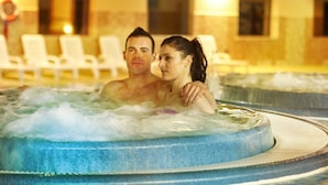Een koppel in een jacuzzi, met een zwembad op de achtergrond.