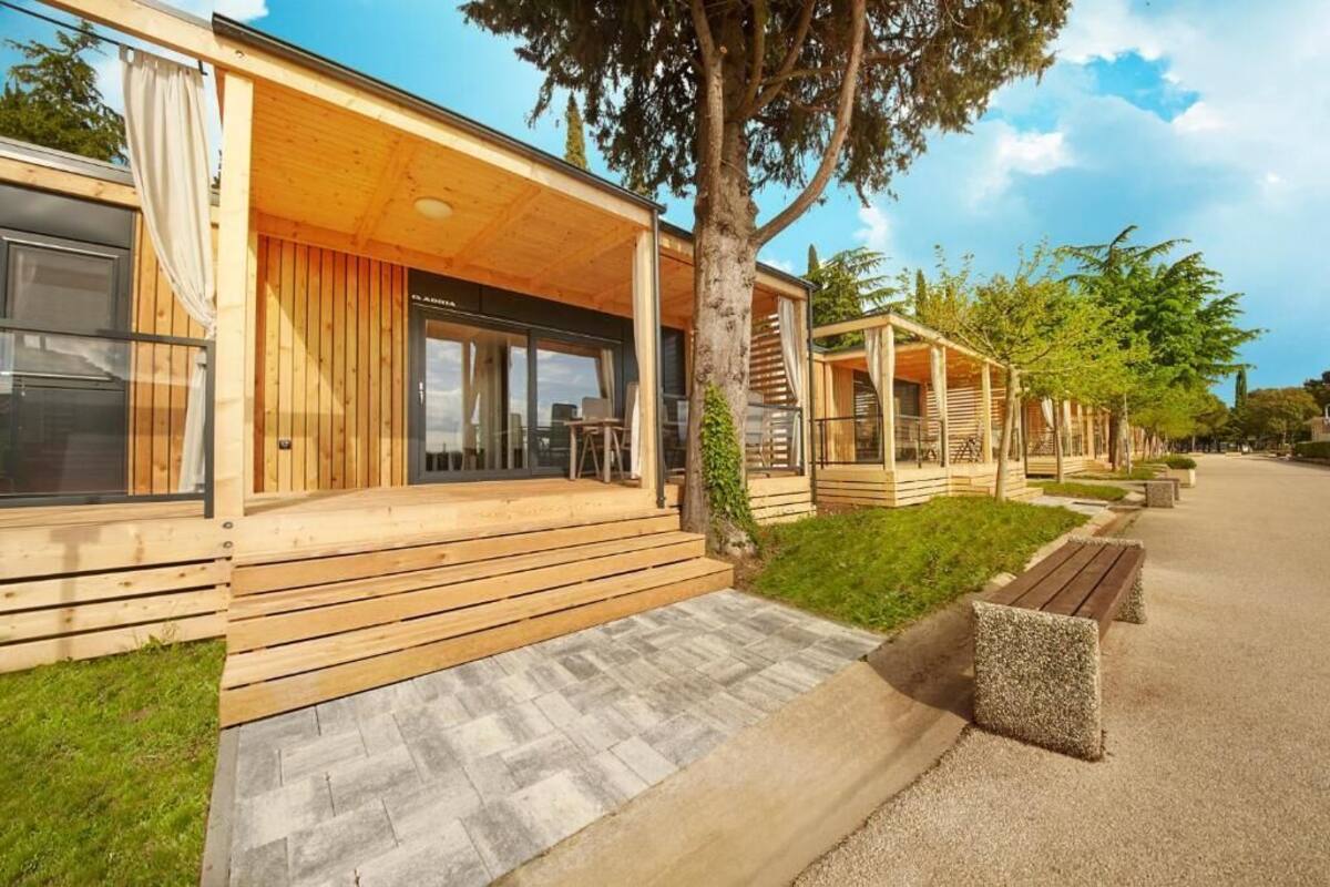 Una hilera de casas móviles de madera con un porche cubierto, un sendero pavimentado y una zona ajardinada.