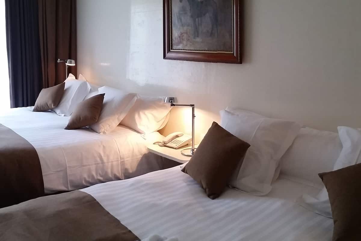 Quarto de hotel com duas camas, mesa de cabeceira com abajur, telefone e um quadro na parede.