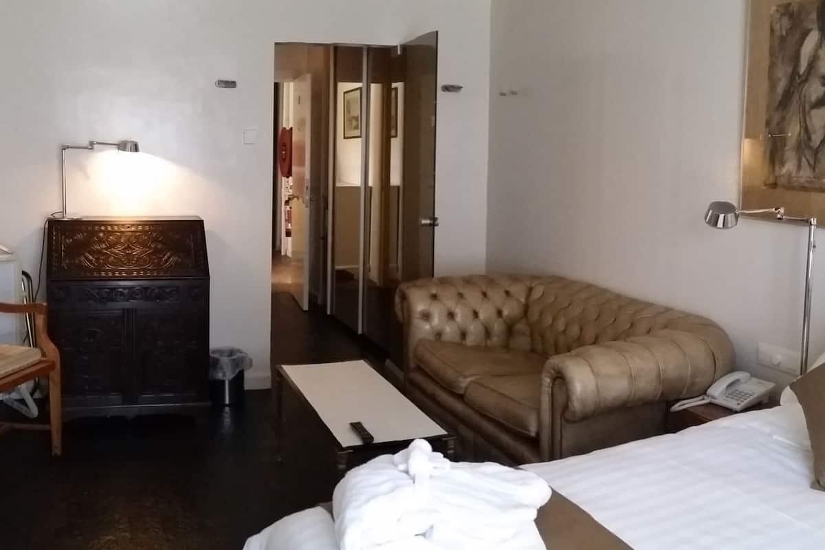 Quarto de hotel com cama, poltrona de couro, escrivaninha com luminária e armário.