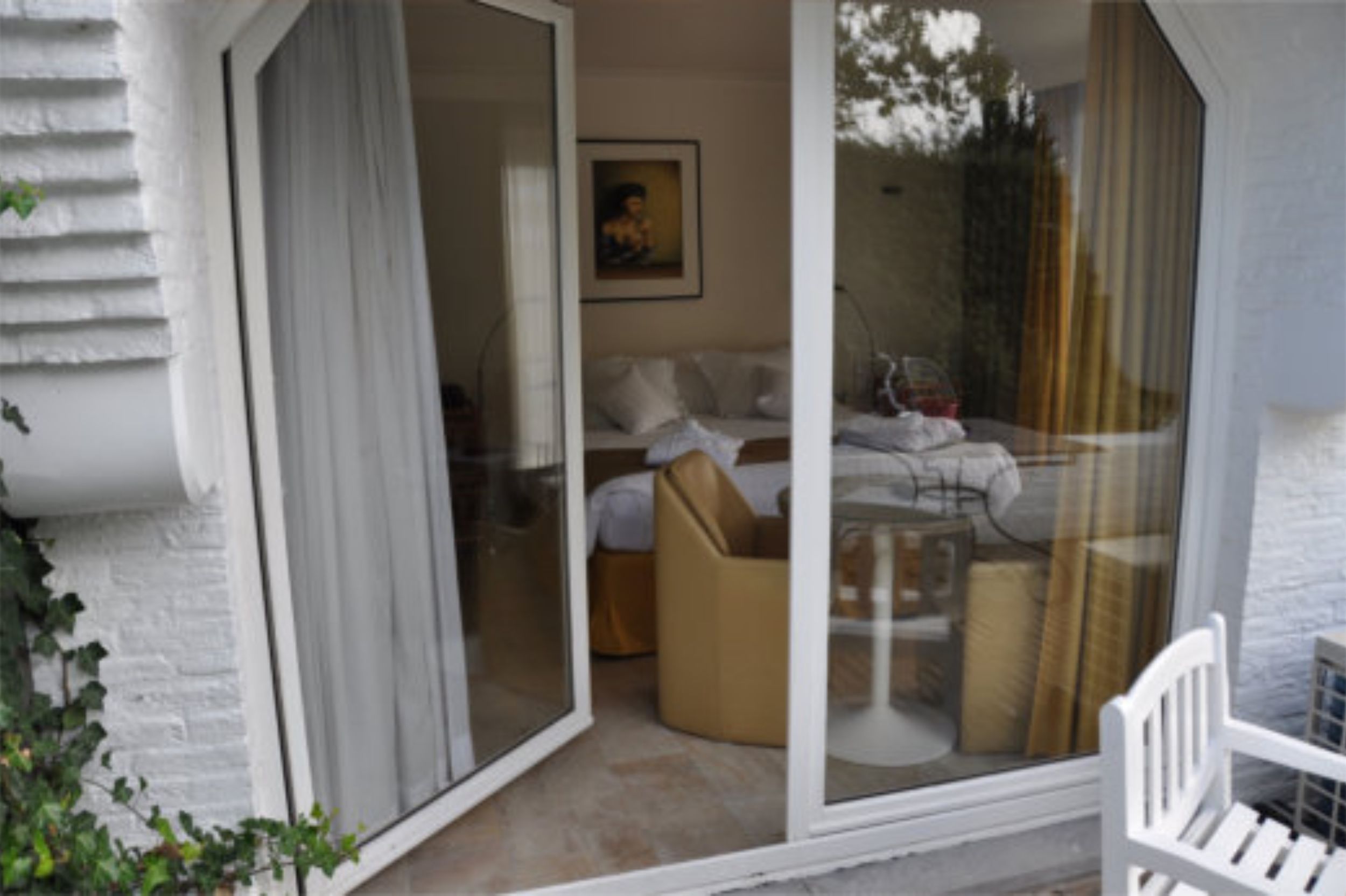 A room with a sliding glass door leading to a balcony, a bed, a chair, and a small table.