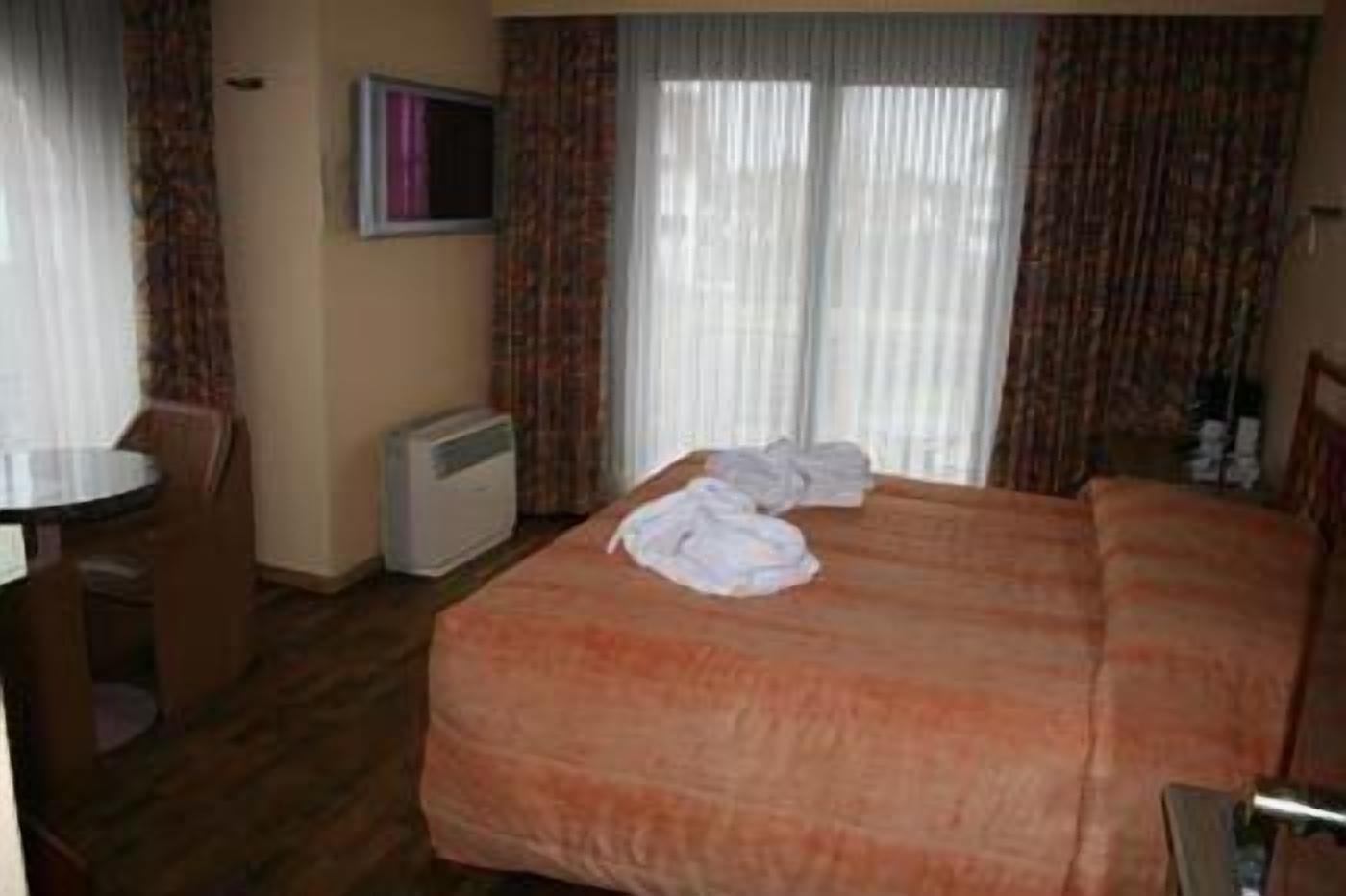 A hotel room with a bed, a desk, a chair, and a television.
