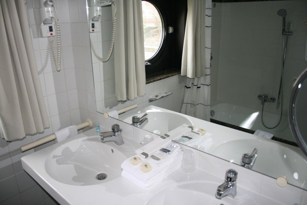 A bathroom with a large sink, a mirror, a shower, and a window.