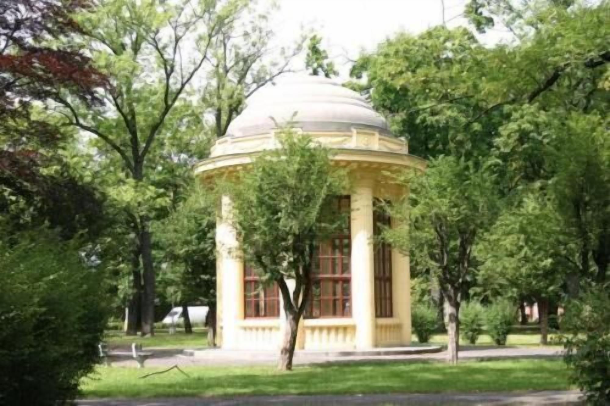 Una edificación aislada con techo abovedado, rodeada de árboles y césped.