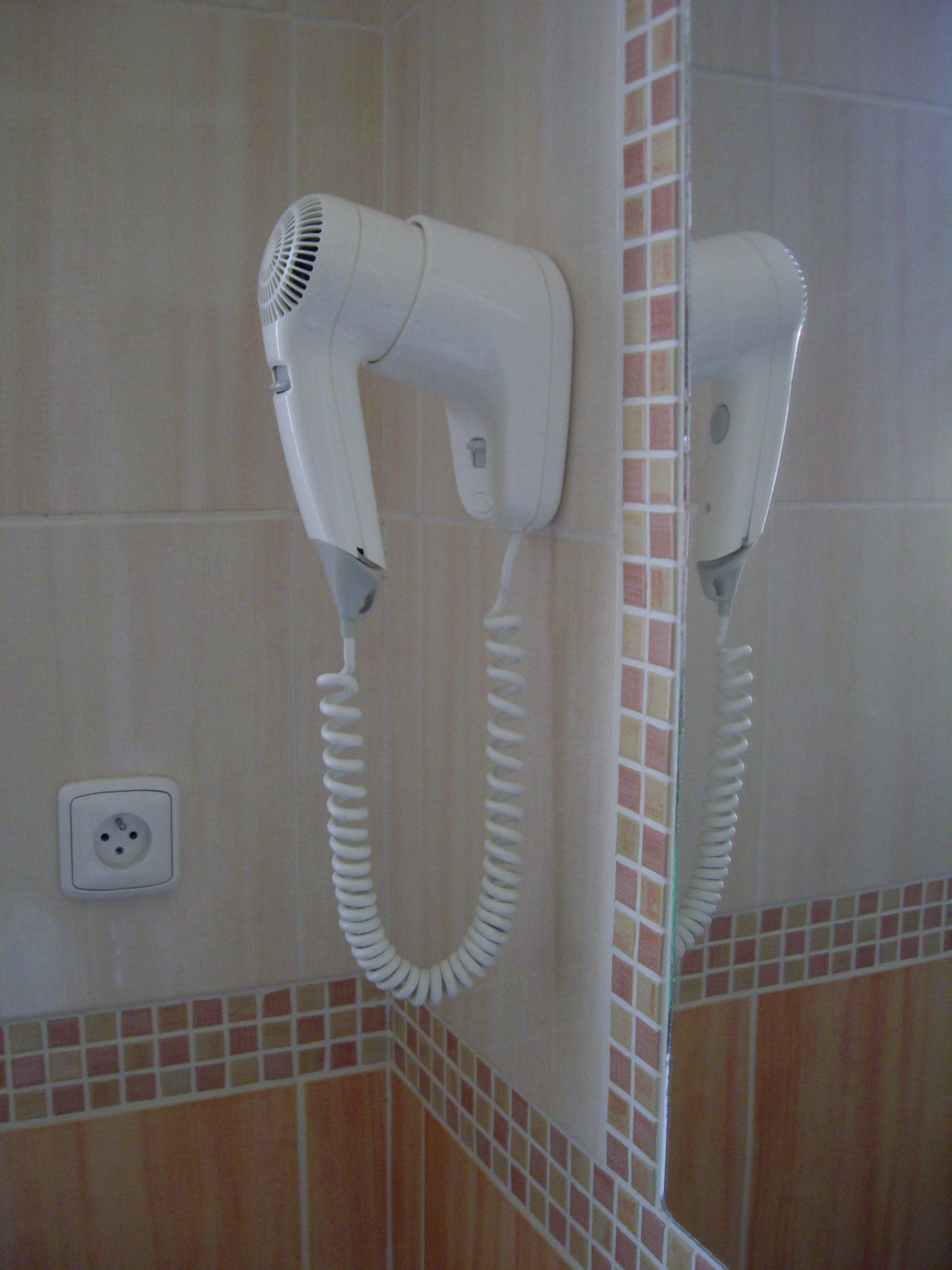 Ein Fön an einer gefliesten Wand, in der Nähe eine Steckdose.