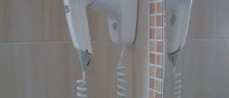 Un secador de pelo fijado a una pared de azulejos, con una toma de corriente cerca.