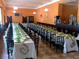 Un salón de banquetes con largas mesas dispuestas para un evento formal, destacando centros de mesa verdes y manteles blancos.