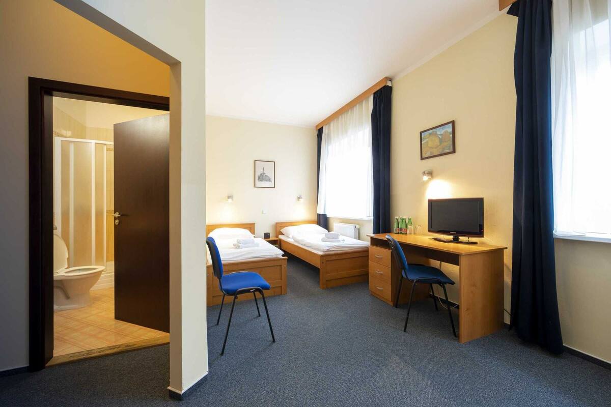 A hotel room with two beds, a desk, a chair, a TV, and a bathroom visible through an open door.