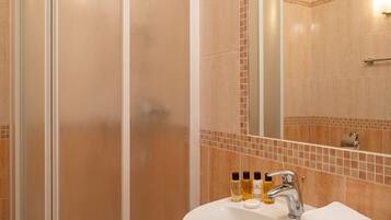Un baño con ducha de vidrio, lavamanos con artículos de aseo y espejo.